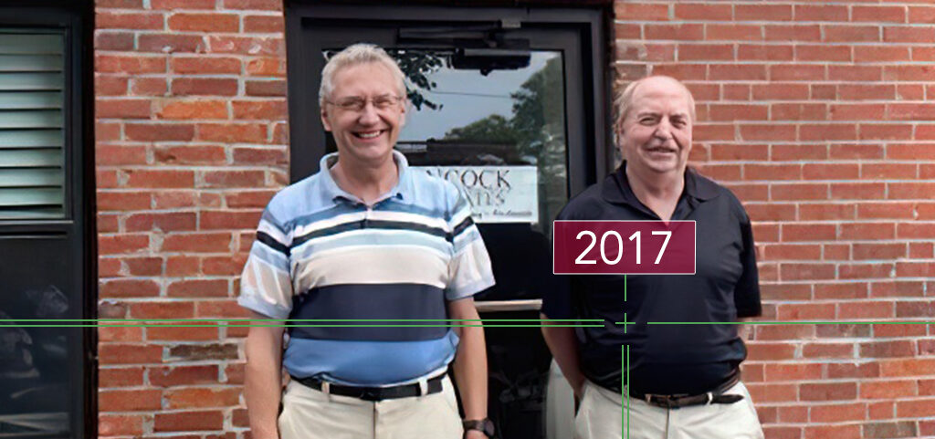 two men in 2017 smiling in front of hancock associates' office